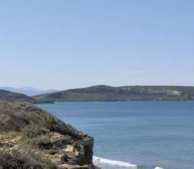 On the left foreground, a promontory covered in small bushes and crowned by the San Giovanni tower, on the right the sea waves with the coastline on the background