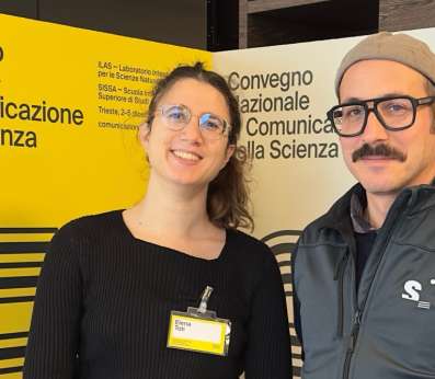 An half-lenght portrait of Elena Toti and Tommaso de Lorenzi, the communicators behind REEForest project's website and social media. Behind them, we can see the yellow panels with the logo of the National Convention of Science Communicators organized in Trieste.